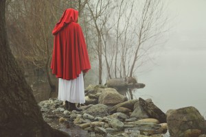 Little red riding hood on a shore of a misty lake . Sadness and surreal concept